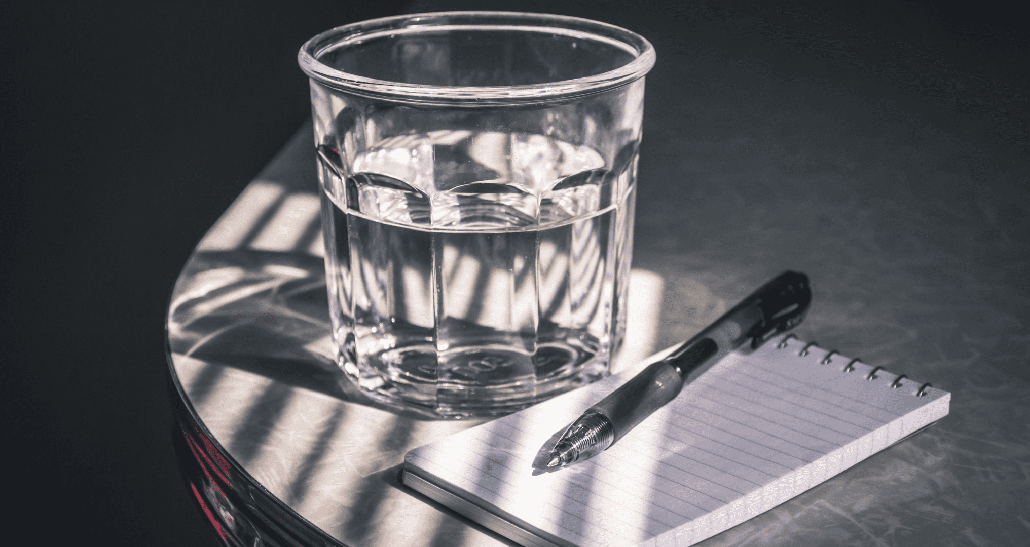 A glass of water beside a pen and a notepad.