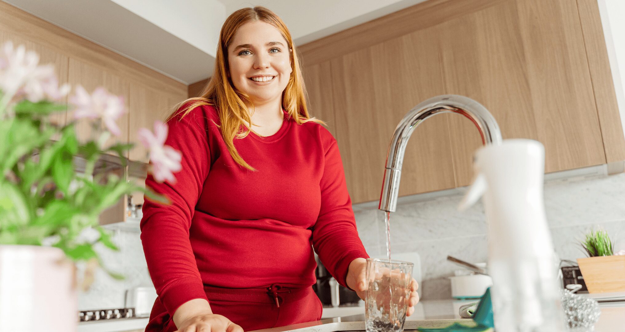 young woman smiling getting water at kitchen faucet
