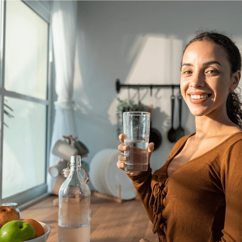 young Latina woman holding a glass of clean water at kitchen sink